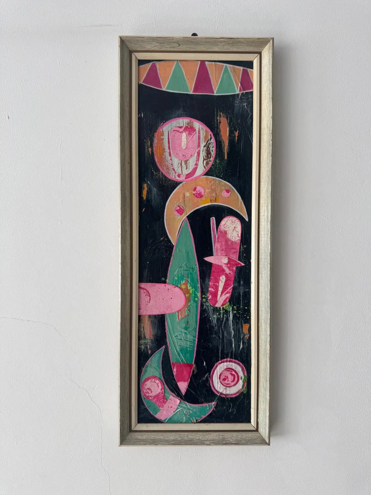 Framed abstract artwork on a white wall above a shelf with books and decor items.
